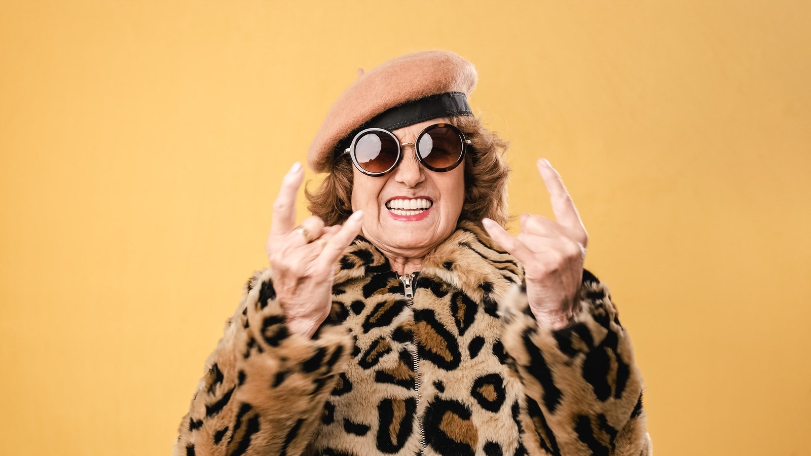 Stylish senior woman showing rock n roll gesture while posing on isolated background.